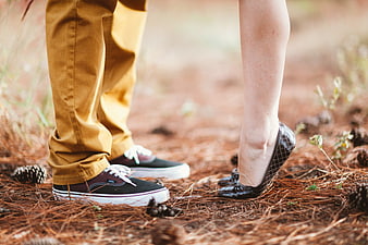 Couple's feet in sneakers and heels on pine needles