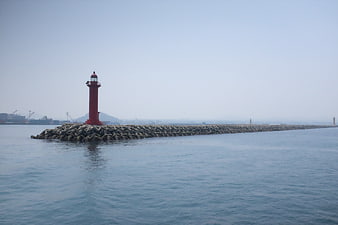 Red Lighthouse on Concrete Breakwater in Hazy Harbor