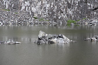 Gray rocks in a quarry lake with steep cliff background