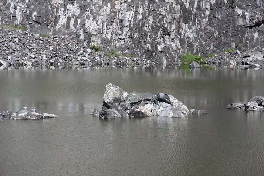 Gray rocks in a quarry lake with steep cliff background