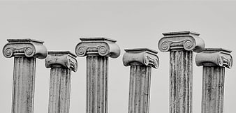 Black and white photo of six classical ionic column tops against a plain sky