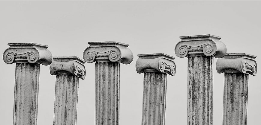 Black and white photo of six classical ionic column tops against a plain sky