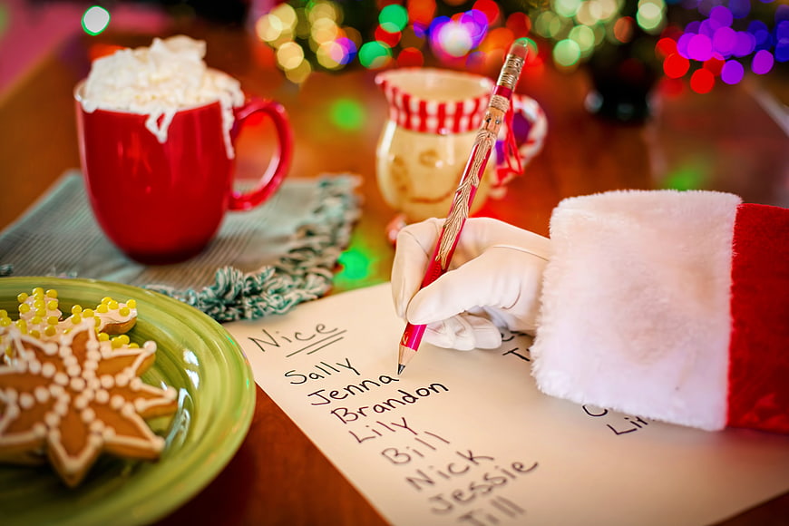 Santa Claus Hand Writing Naughty Or Nice List With Holiday Decor