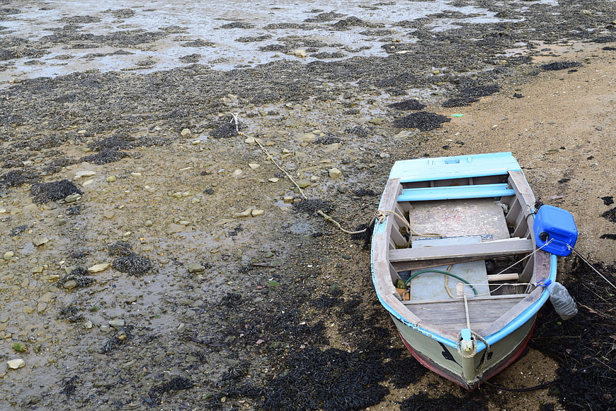 Small wooden boat resting on muddy tidal beach