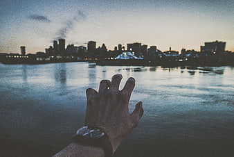 Man's Hand with Watch Reaching Toward City Skyline at Dusk