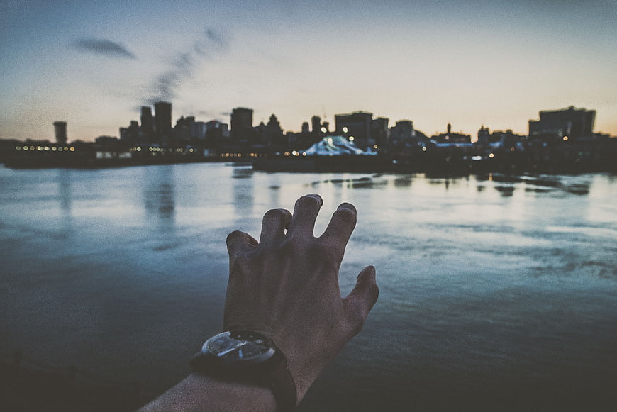 Man's Hand with Watch Reaching Toward City Skyline at Dusk