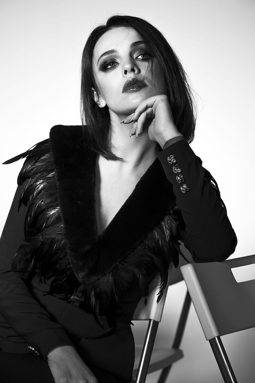 Black and white studio portrait of a young woman in a feathered jacket