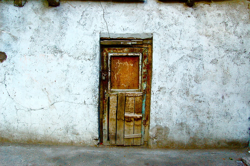 Old weathered wooden door in cracked white wall
