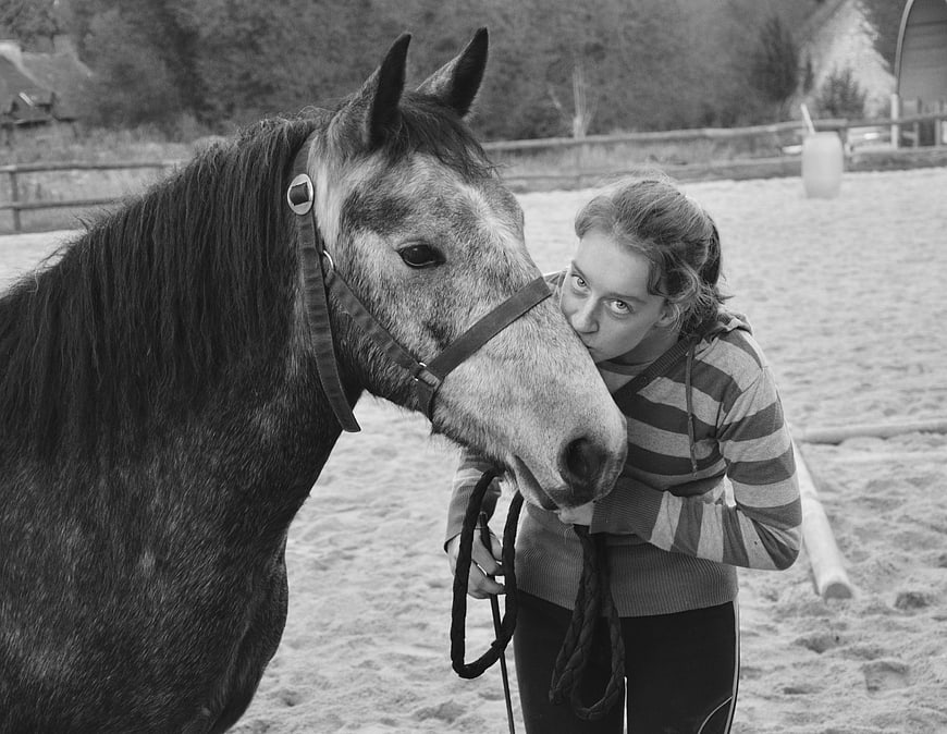 Black and white photo of young woman kissing horse