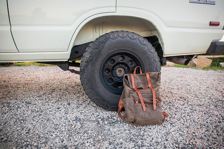 Vintage Backpack Leaning Against Off-Road Vehicle Tire