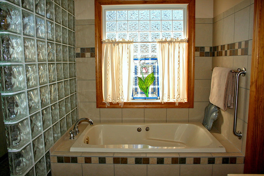 Spacious bathroom with glass block wall and stained glass window