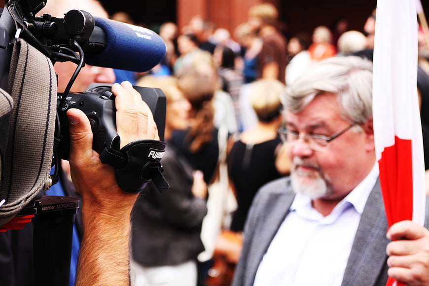 Journalist filming man with flag at public event