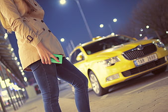 Woman waiting for yellow taxi at night with smartphone