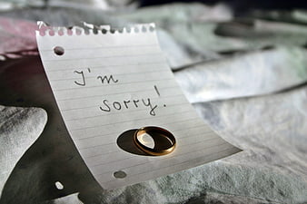 Gold wedding ring on a handwritten 'I'm sorry' note on a bed