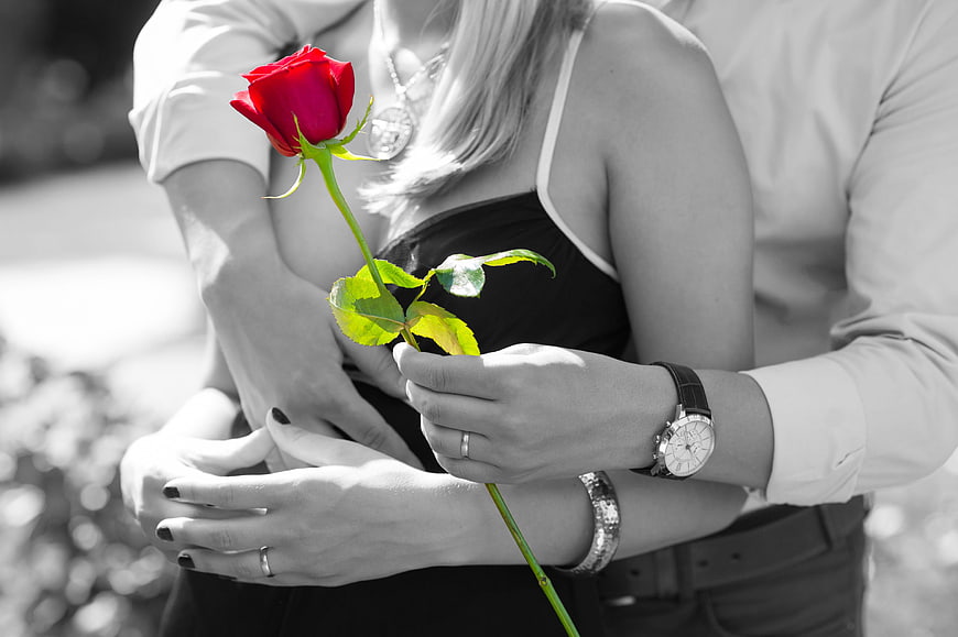 Romantic couple embracing with a single red rose in black and white