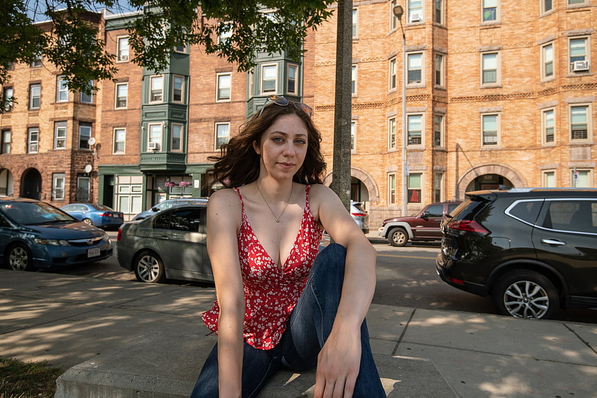 Young woman in red floral top sitting on city sidewalk