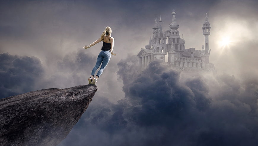 Woman balancing on cliff edge facing fantasy castle in clouds