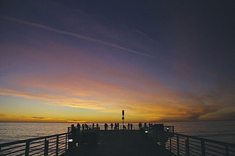 Silhouetted People on Pier at Sunset Over Ocean