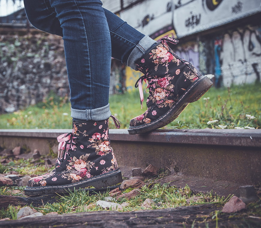 Woman wearing floral boots on train tracks with graffiti background