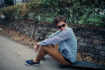 Stylish Young Man Sitting on Skateboard with Sunglasses
