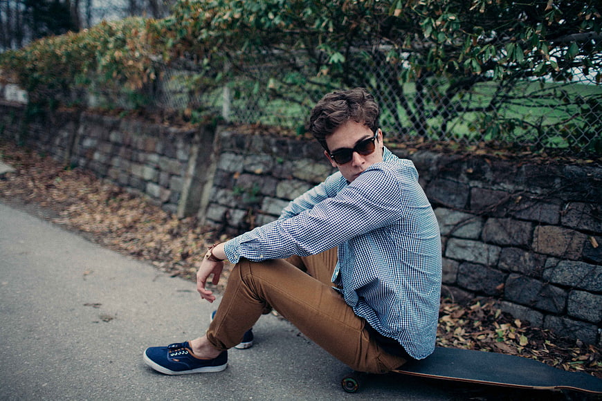 Stylish Young Man Sitting on Skateboard with Sunglasses