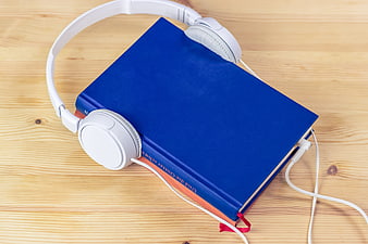White headphones resting on a blue hardcover book on a wooden table