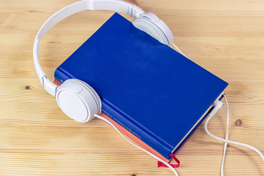 White headphones resting on a blue hardcover book on a wooden table