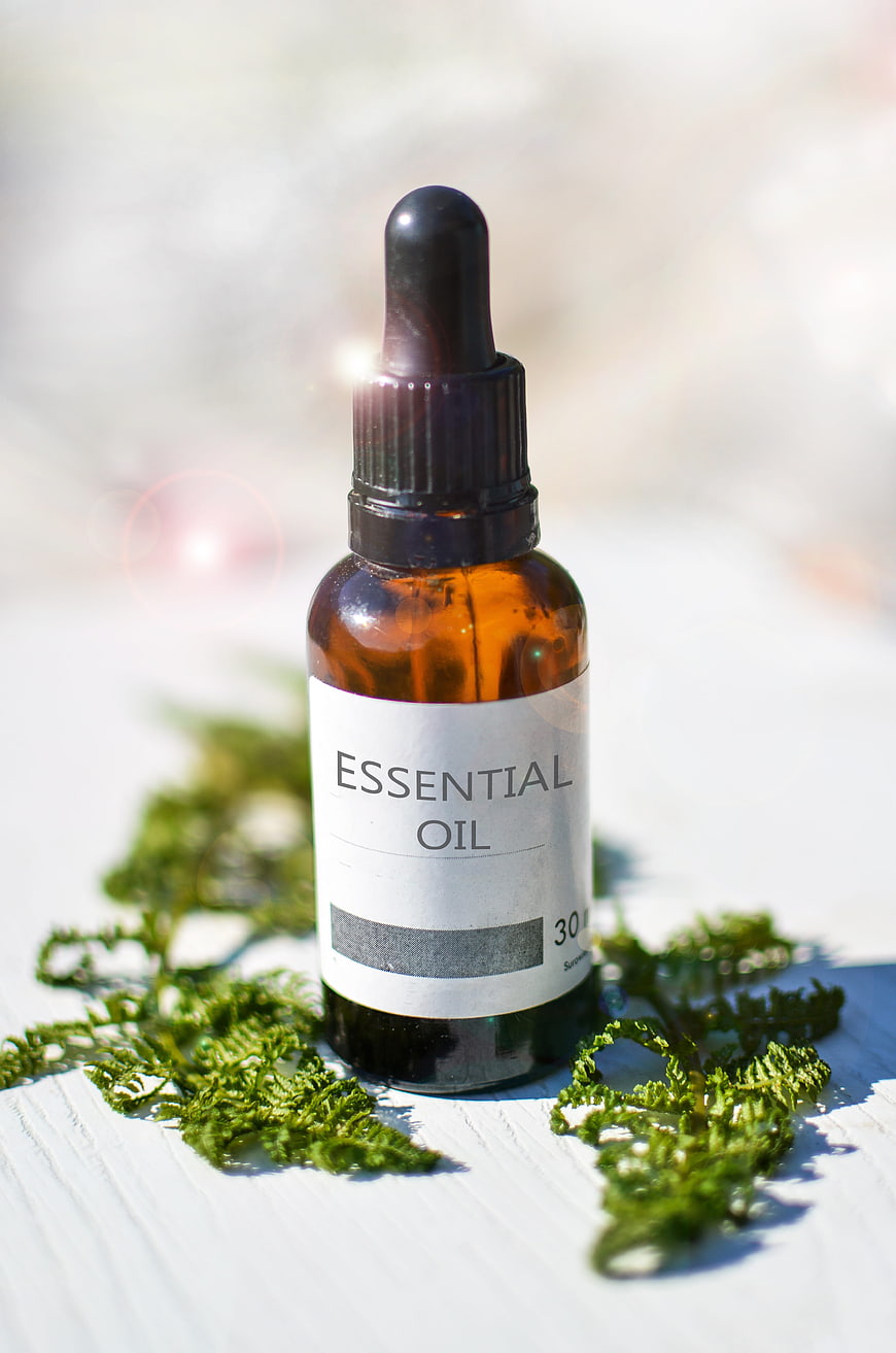 Amber Essential Oil Bottle with Ferns on White Wood