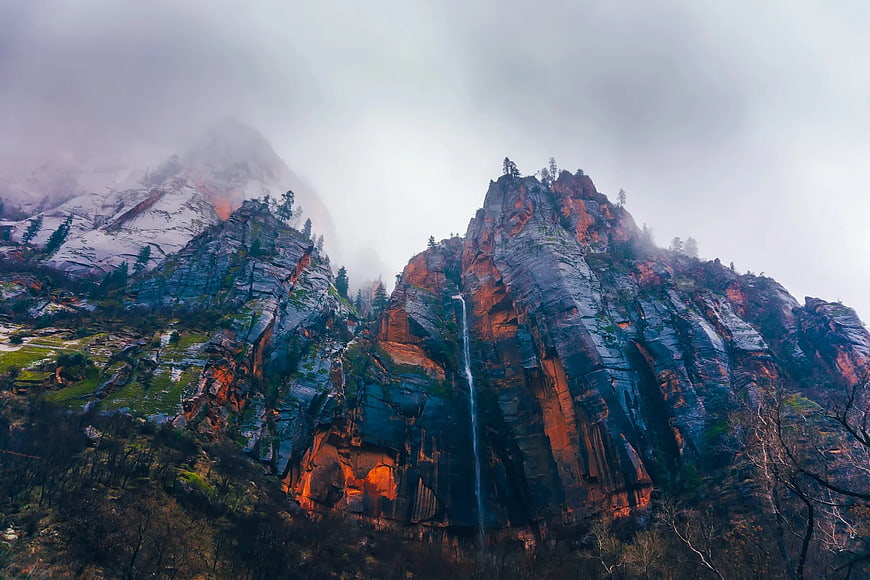 Misty waterfall cascading down rugged red rock mountain cliffs
