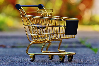 Golden miniature shopping cart on asphalt with blurred background
