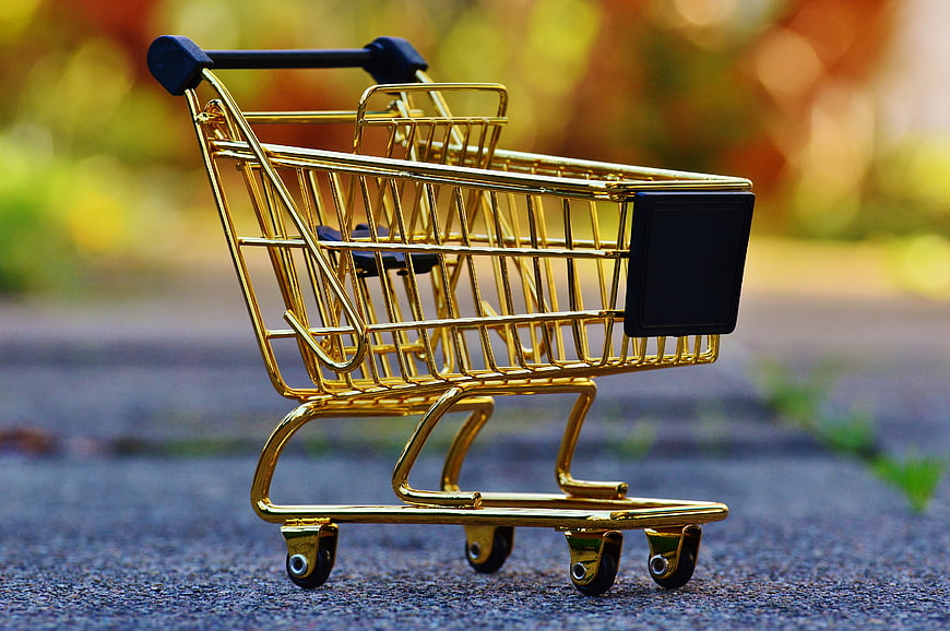 Golden miniature shopping cart on asphalt with blurred background