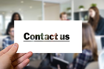 Hand holding card with contact us text blurred office background