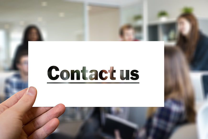 Hand holding card with contact us text blurred office background