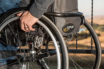 Close-up of elderly man's hand gripping wheelchair wheel outdoors