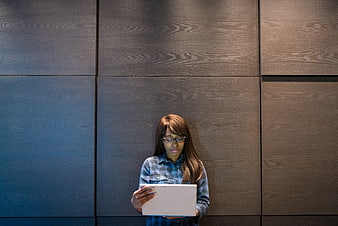 Woman with glasses using tablet against wood wall