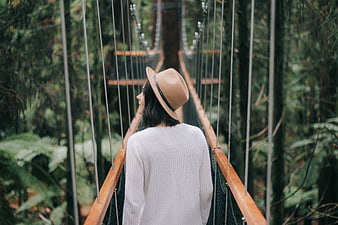 Woman in Hat Walking on Forest Suspension Bridge