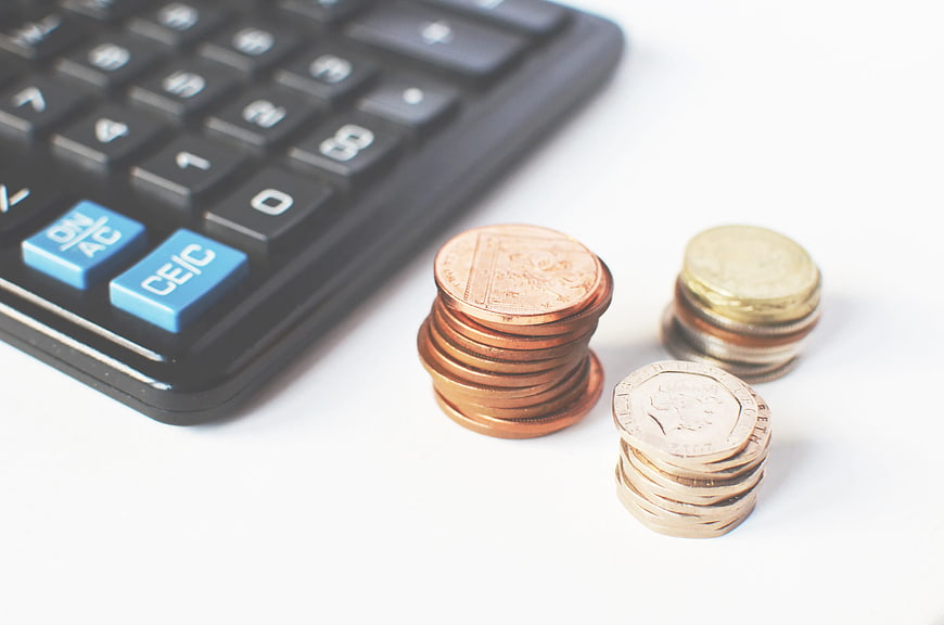 Stacks of coins next to a calculator on white background