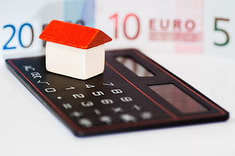 Miniature house on calculator with euro banknotes background