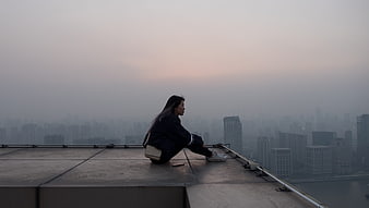 Woman sitting on rooftop overlooking foggy city skyline at dusk