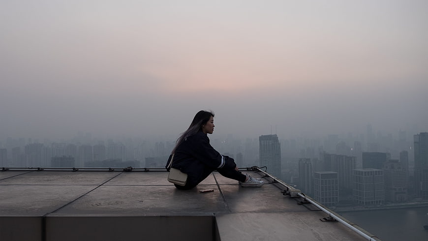Woman sitting on rooftop overlooking foggy city skyline at dusk