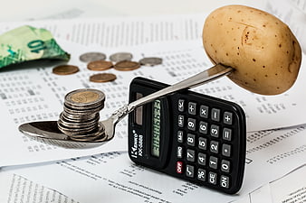 Potato and coins balanced on spoon over calculator