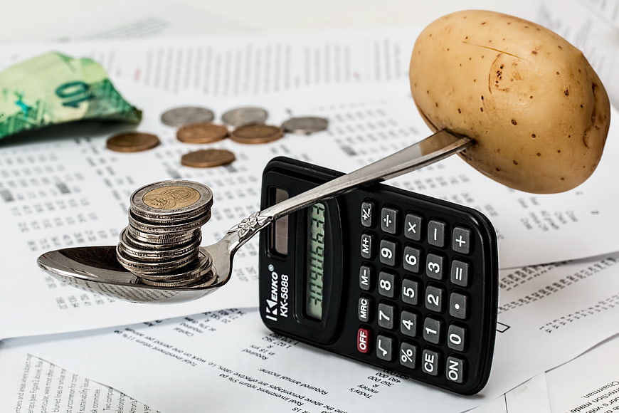 Potato and coins balanced on spoon over calculator