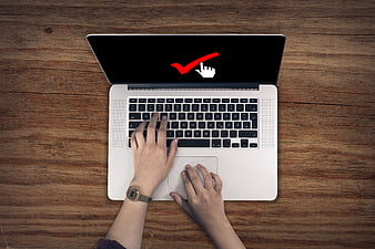 Top view of hands typing on laptop with checkmark on screen