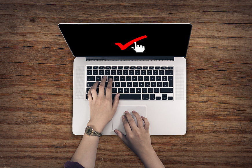 Top view of hands typing on laptop with checkmark on screen