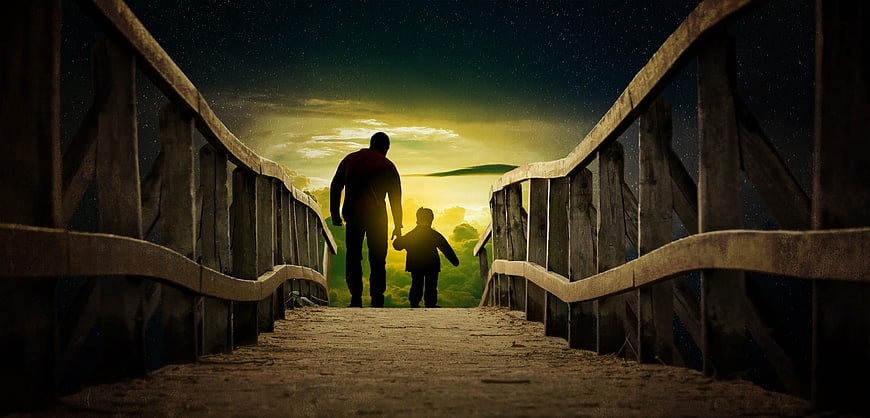 Father and son walking on wooden bridge at sunset
