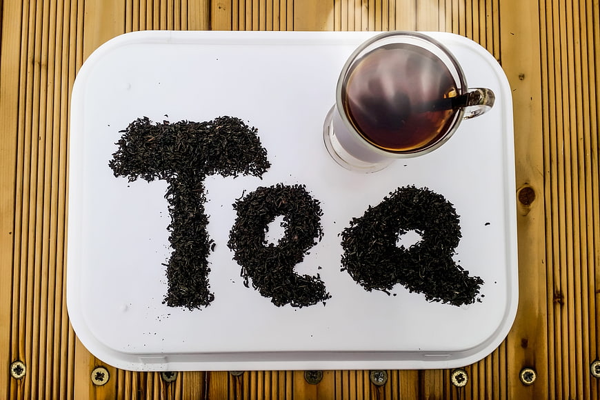 Top view of tea leaves spelling Tea on white tray