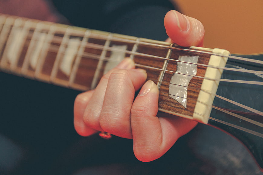 Close-up of hand playing acoustic guitar fretboard