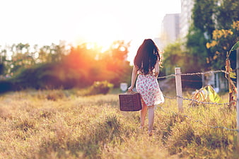 Woman in floral dress walking away with basket at sunset