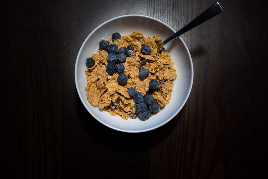 Overhead view of cereal bowl with blueberries on dark wood