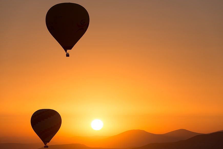 Hot Air Balloons Silhouette Against Golden Sunrise Over Mountains